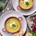 Two bowls of creamy broccoli soup topped with sliced almonds, parsley and a swirl of cream.