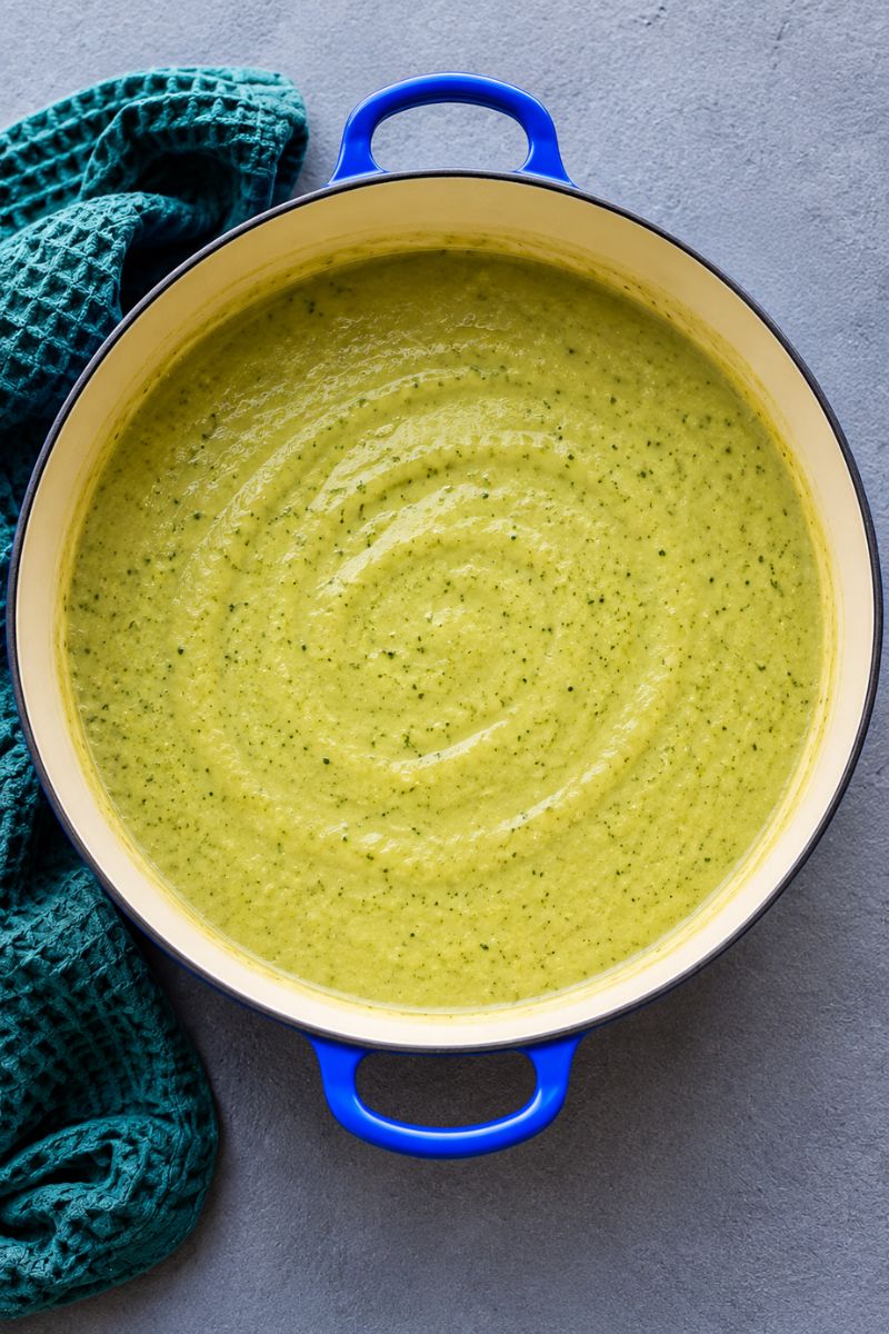 Smooth, creamy broccoli soup blended in a blue-handled pot.