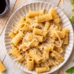 Overhead view of creamy rigatoni cacio e pepe pasta topped with freshly grated Pecorino Romano and cracked black pepper.