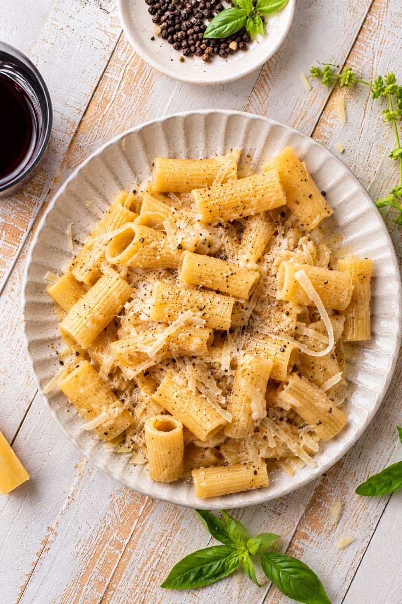 Overhead view of creamy rigatoni cacio e pepe pasta topped with freshly grated Pecorino Romano and cracked black pepper.