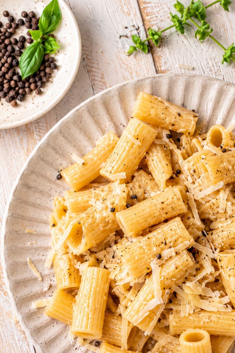Close-up of rigatoni pasta coated in a creamy Pecorino Romano cheese sauce with freshly cracked black pepper.