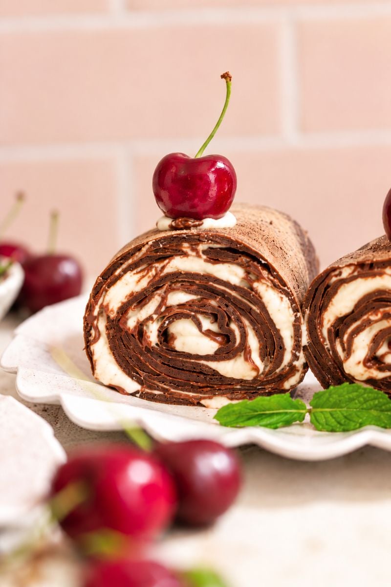 Chocolate crepe roll filled with Nutella and whipped cream, topped with a fresh cherry.