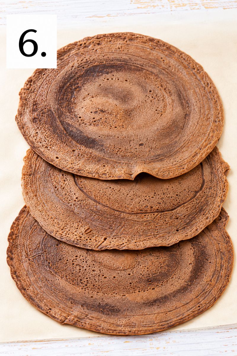 Three homemade chocolate crepes overlapping on a light-colored surface.