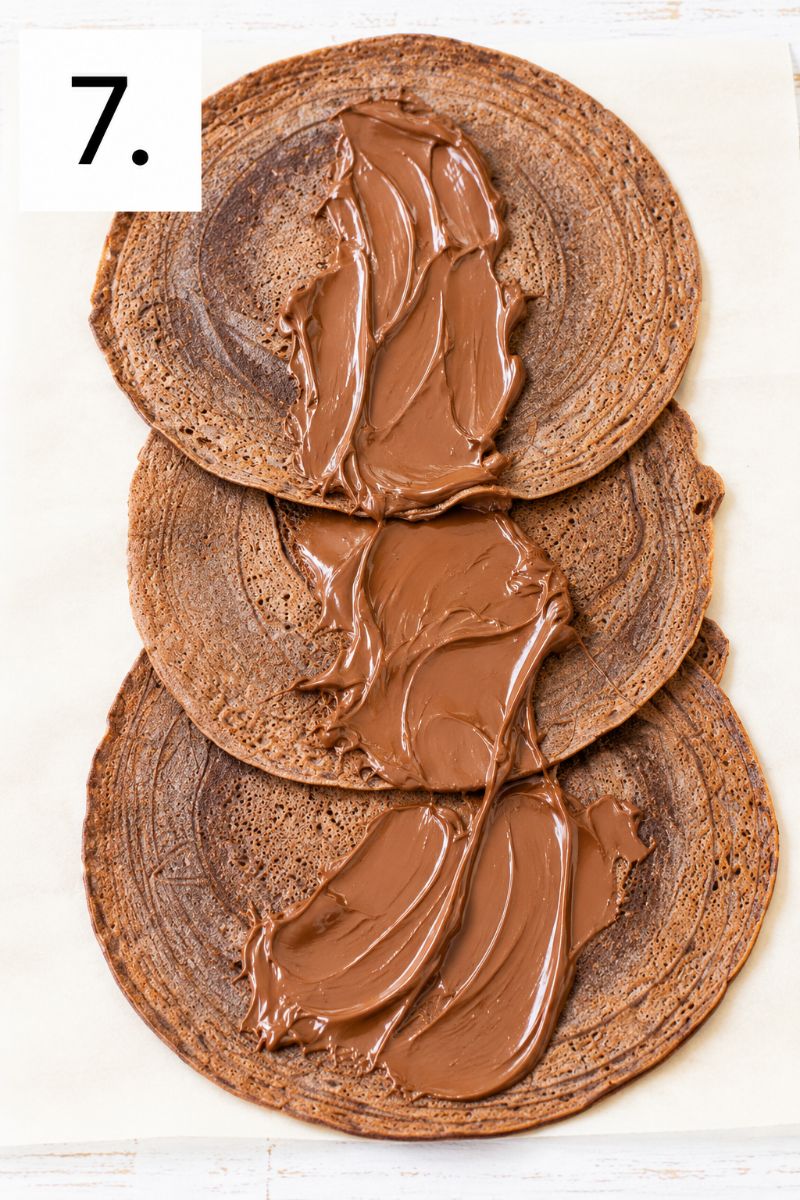 Nutella spread over three overlapping chocolate crepes before adding whipped cream.