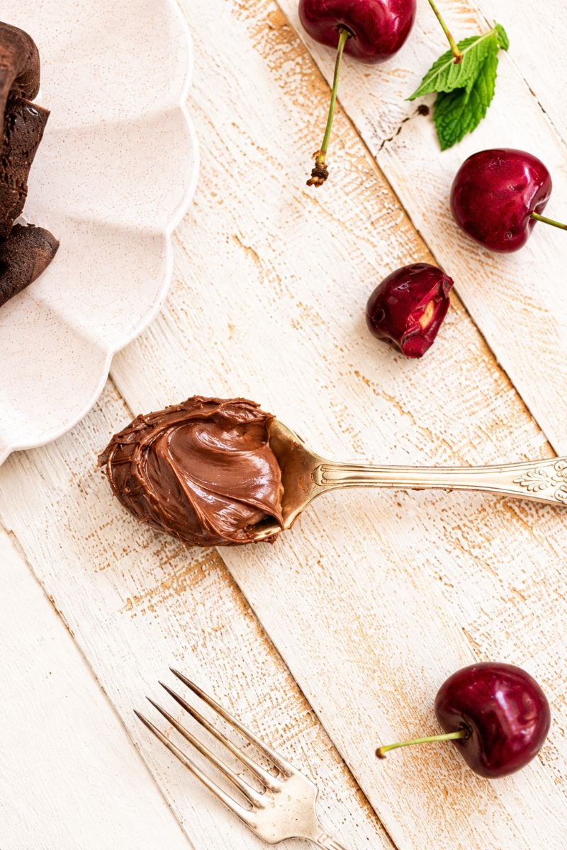 Spoon coated with creamy Nutella on a rustic wooden surface beside fresh cherries.
