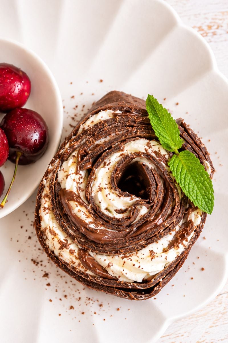 Chocolate crepe roll with layers of whipped cream and Nutella, served with fresh cherries and mint.