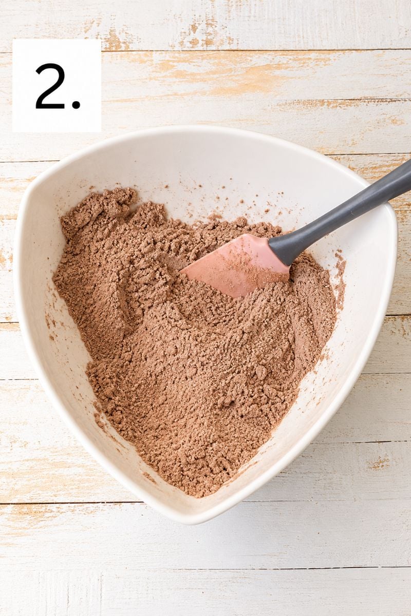 Flour and cocoa powder combined in a white mixing bowl with a spatula.
