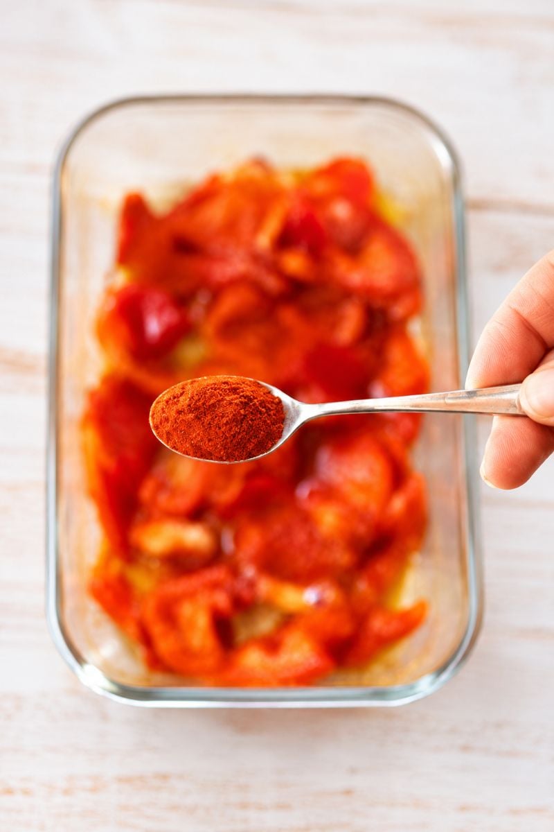 A teaspoon of smoked paprika held above chopped red peppers, ready to season them before roasting.