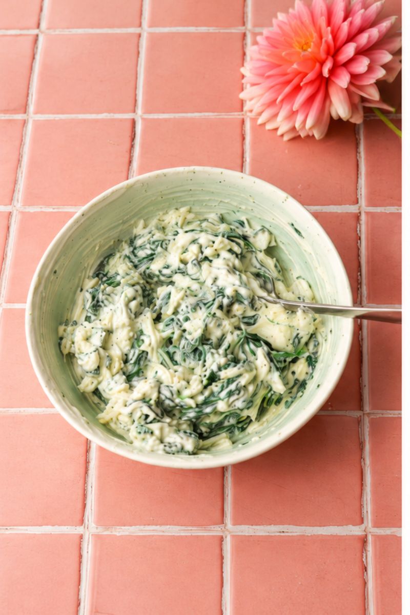 Cooked spinach mixed with cream cheese and shredded cheese in a bowl.