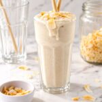Creamy coconut shake with toasted coconut flakes in a tall glass.