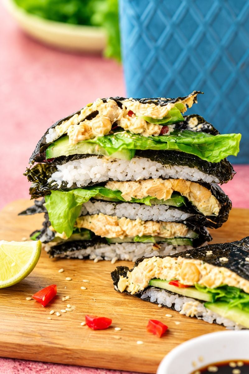 Homemade chickpea sushi wraps stacked on a wooden board with fresh vegetables and creamy filling.