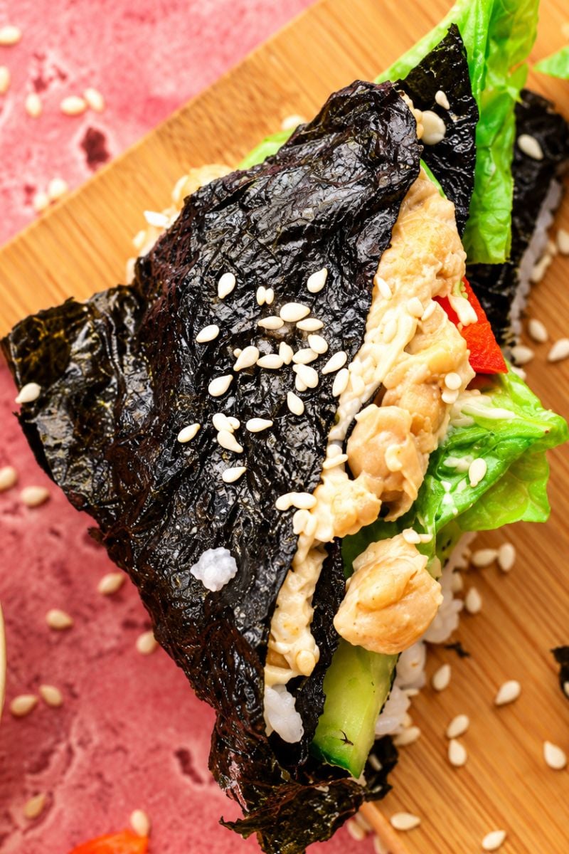 Close-up of a homemade nori sushi wrap filled with mashed chickpeas, cucumber, lettuce, and sushi rice.
