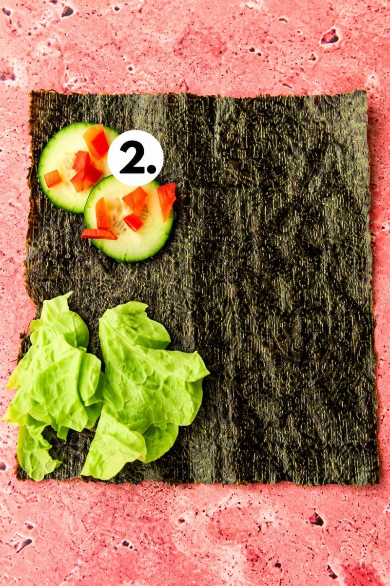 Sliced cucumber and red capsicum arranged on a nori sheet with fresh lettuce.