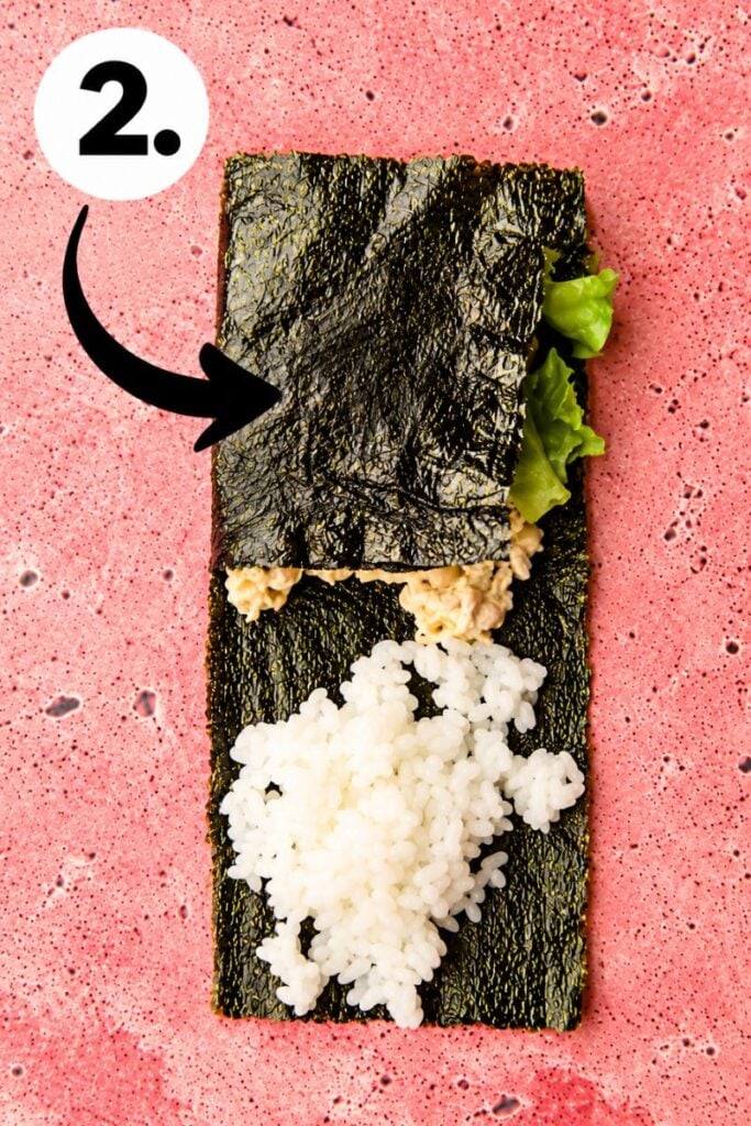 Second fold: Folding the nori sheet over the vegetable filling and sushi rice to form a compact wrap.