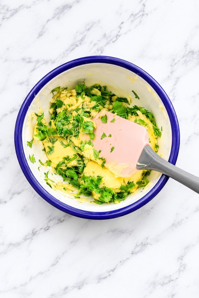 Softened butter mixed with minced garlic and fresh parsley in a bowl for cheesy stuffed garlic bread.