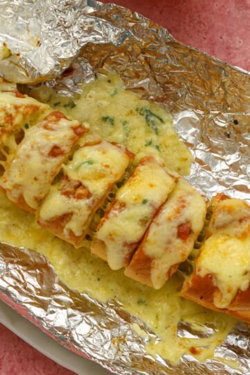 Stuffed homemade garlic bread with melted cheese in tin foil.
