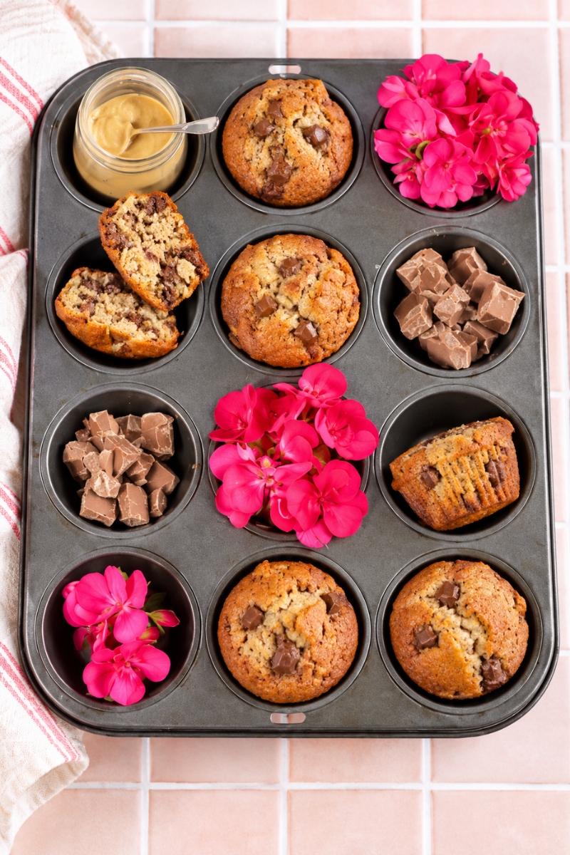Homemade banana chocolate chunk muffins in a muffin tin with chocolate pieces and pink flowers.