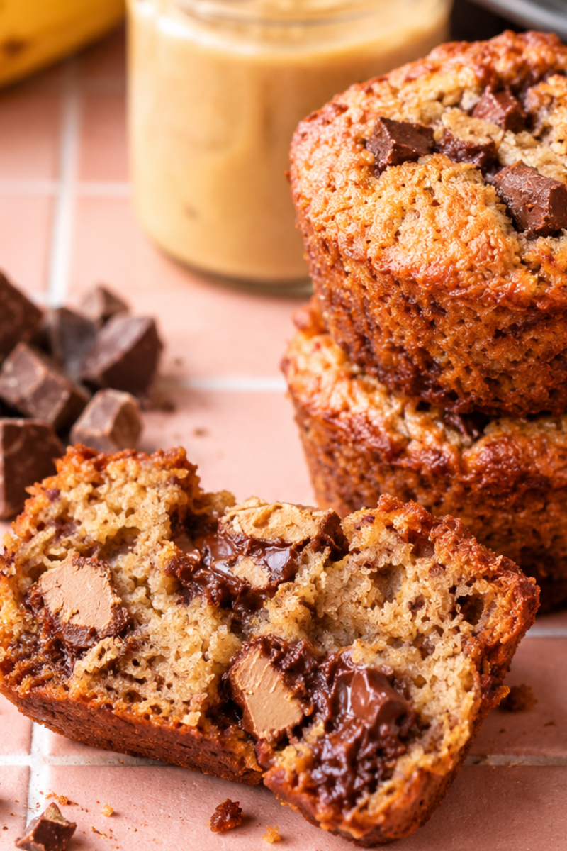 Stacked banana chocolate chunk muffins with a cut muffin showing chocolate pieces inside.