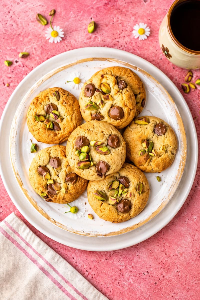 Homemade pistachio chocolate chip cookies topped with chopped pistachios and chocolate chips on a white plate.