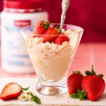 Creamy protein rice pudding topped with fresh strawberries and cream in a glass dessert bowl.
