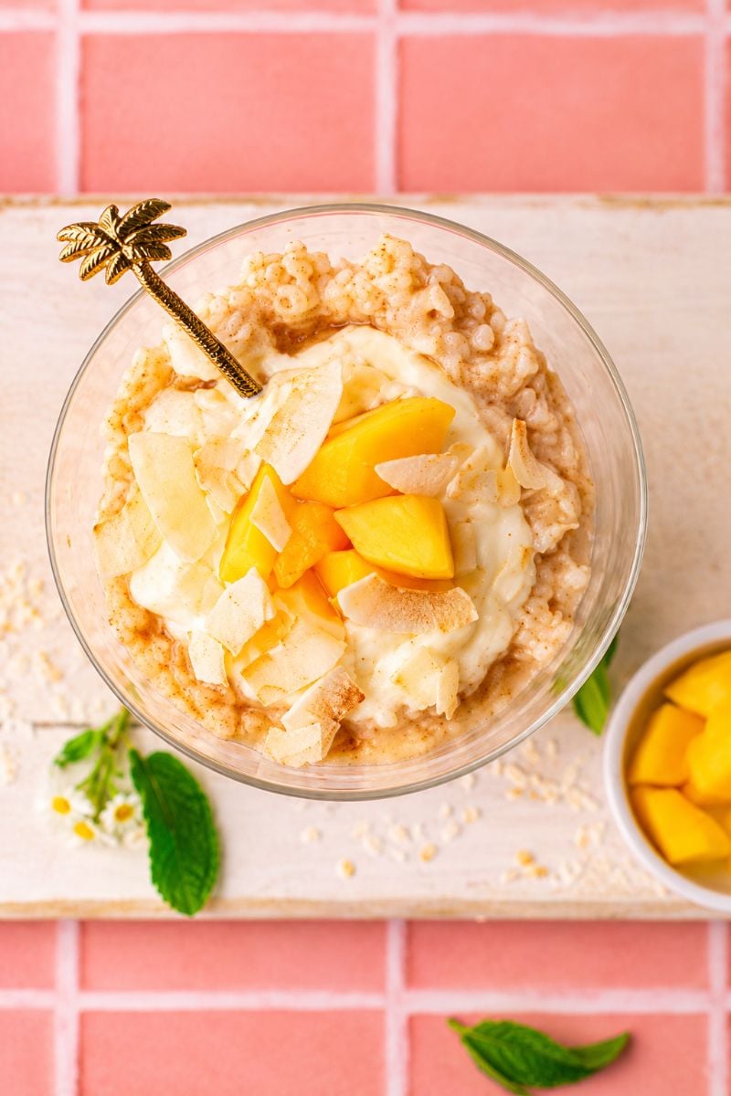 Overhead view of vanilla protein rice pudding with mango pieces, creamy yogurt, and coconut flakes.