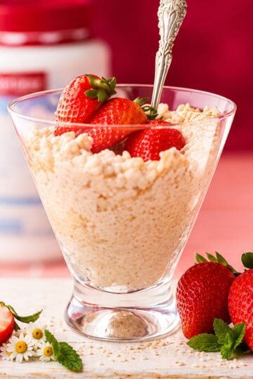 Creamy protein rice pudding topped with fresh strawberries and cream in a glass dessert bowl.