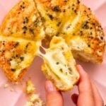 Hand holding a piece of golden stuffed bagel filled with warm, creamy cheese.