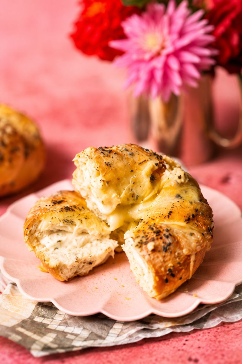 Cream cheese stuffed bagel served on a pink plate with dipping sauce on a pink background.