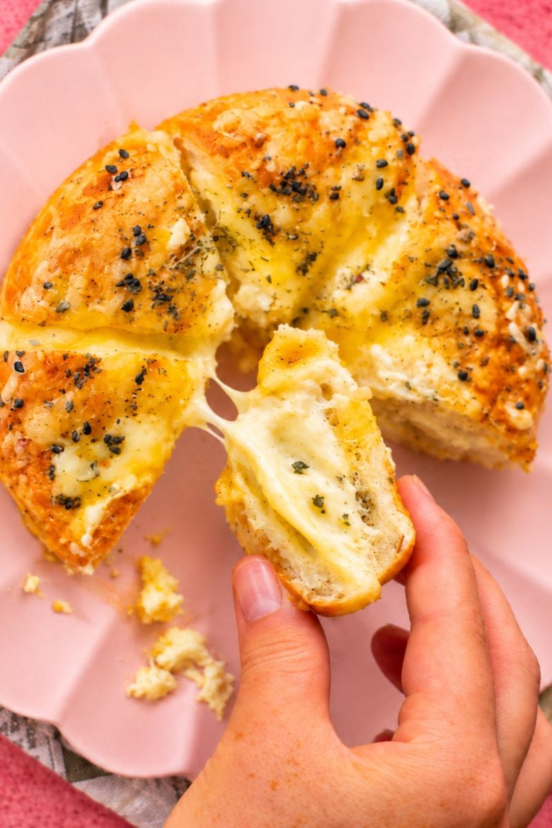 Hand holding a piece of golden stuffed bagel filled with warm, creamy cheese.