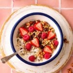 Homemade sugar free granola topped with fresh strawberries and raspberries, served with milk in a white bowl.