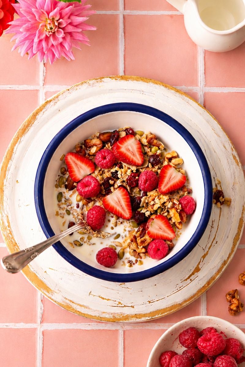 Homemade sugar free granola topped with fresh strawberries and raspberries, served with milk in a white bowl.