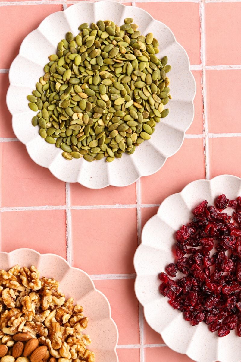 Pumpkin seeds, walnuts and dried cranberries arranged in bowls for homemade sugar free granola.