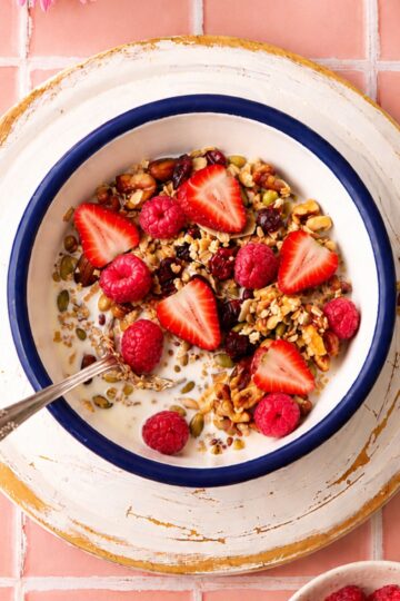 Homemade sugar free granola topped with fresh strawberries and raspberries, served with milk in a white bowl.