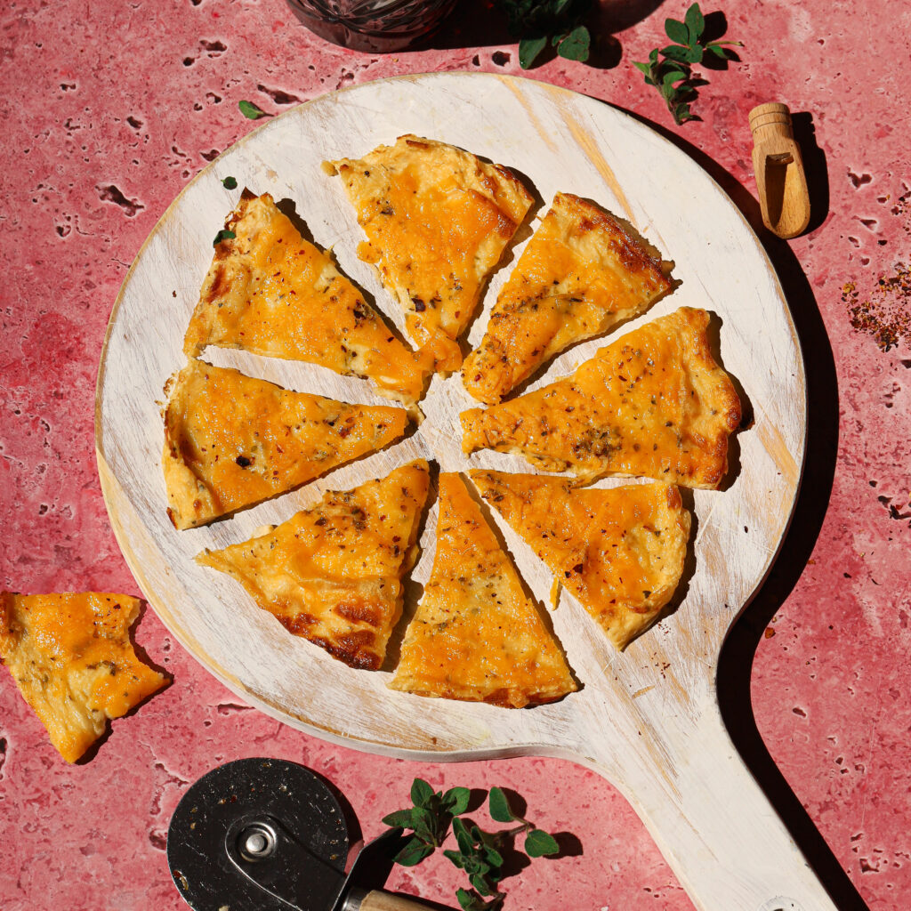 Cottage cheese pizza on a white board with a pizza cutter and a drink to the side.