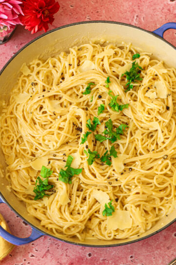 Spaghetti with Alfredo in a pan with grated cheese and garnished with parsley.