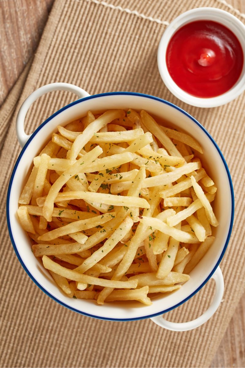A bowl of french fries and ketchup on the side.