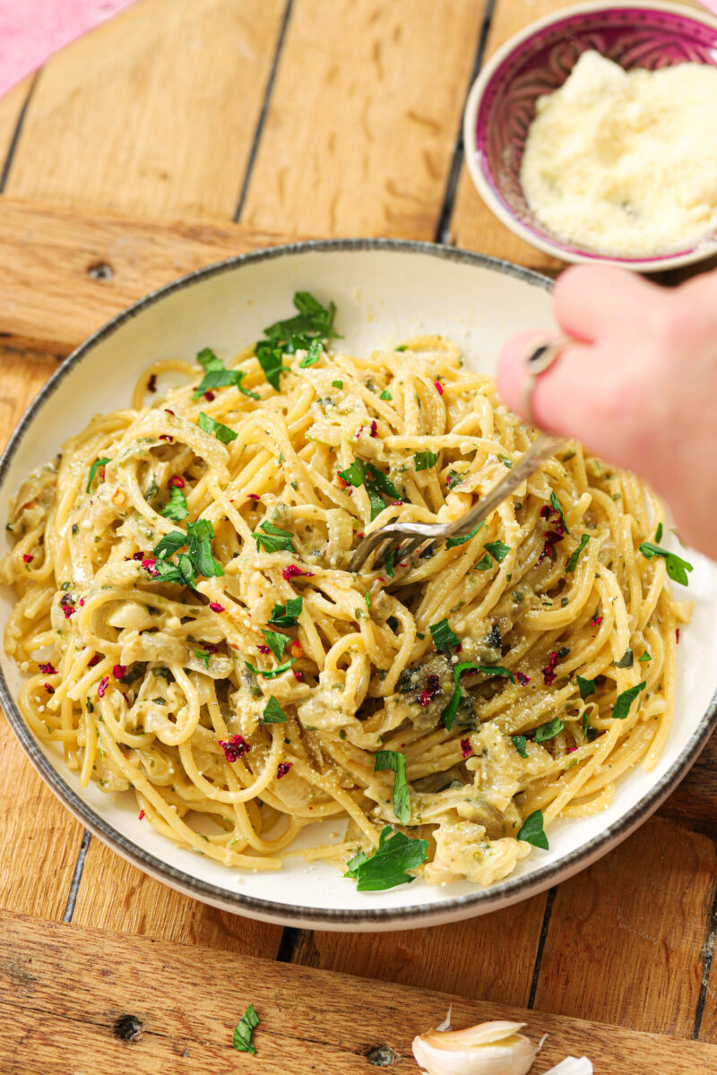 A bowl of French onion pasta with a hand sprinkling parmesan cheese on the side.