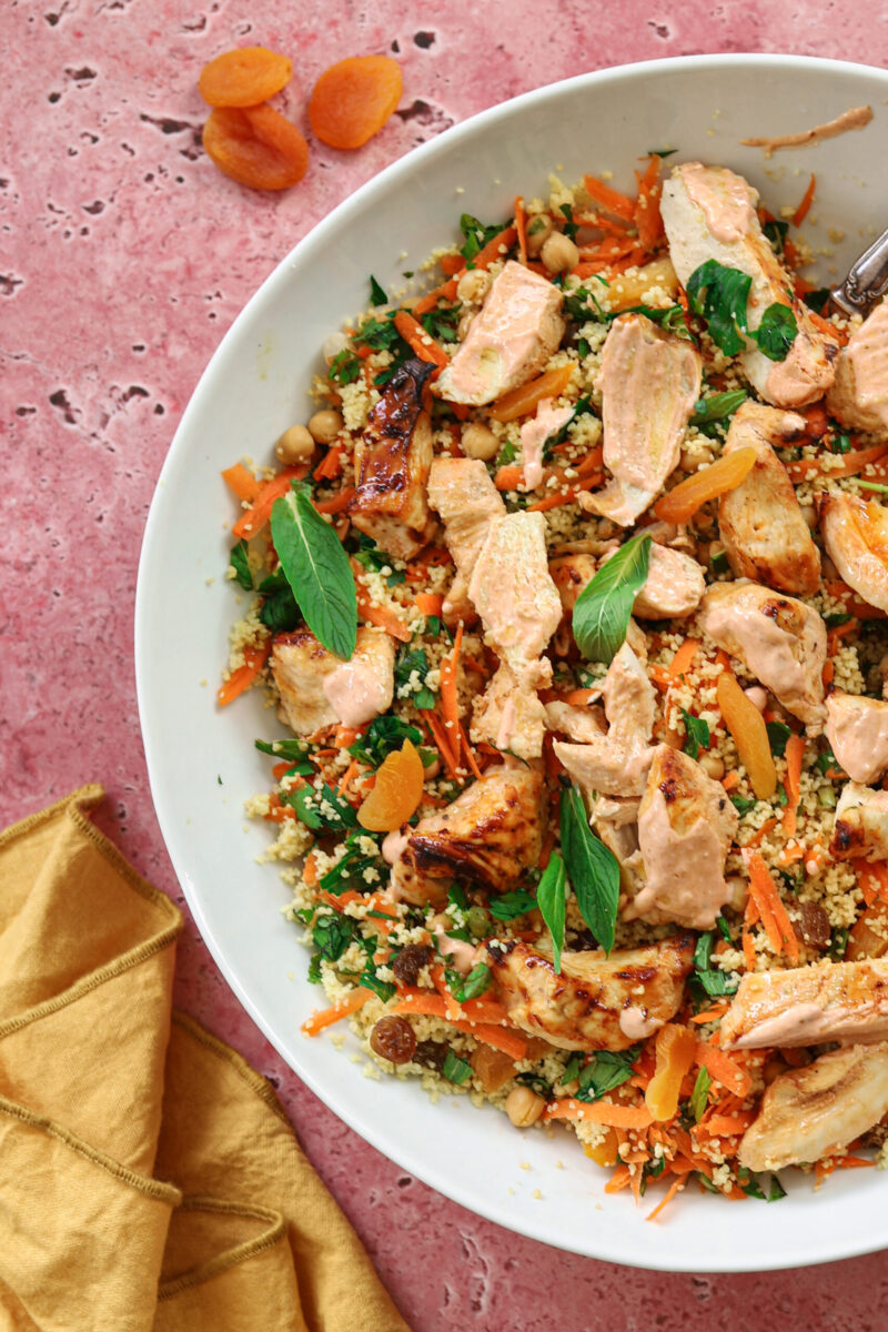 Sliced harissa chicken on couscous with herbs and a dressing. 