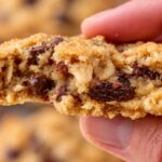 Soft and chewy oatmeal raisin chocolate chip cookie broken in half to show the chocolate chips and raisins inside.