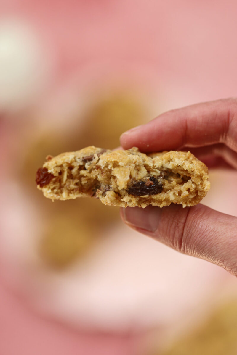 Holding an oatmeal raisin chocolate chip cookie that is in half and you can see the soft, chewy centre. 