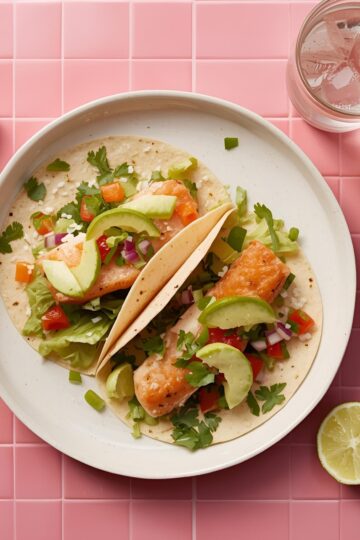 Fish tacos on a plate with sliced lime and a glass of iced water on the side.