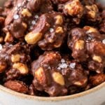 Homemade chocolate nut clusters with almonds and cashews in a ceramic bowl, topped with flaky sea salt.