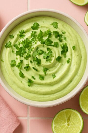 A bowl of avocado lime crema with slices of lime wedges on the side.