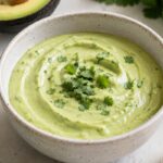 A bowl of avocado lime crema. With avocado and lime next to the bowl.