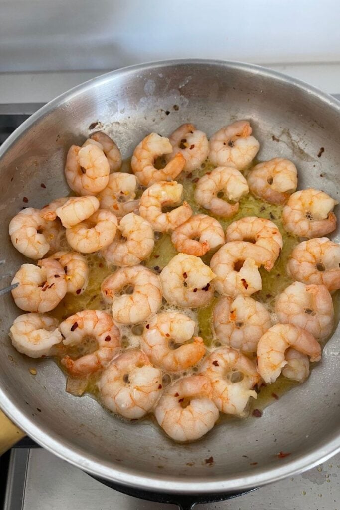Pink shrimp cooked in a frying pan with butter and red pepper flakes.