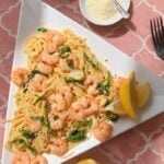 Creamy garlic butter shrimp pasta with spaghetti, baby spinach, Parmesan cheese, and red pepper flakes on a white plate.