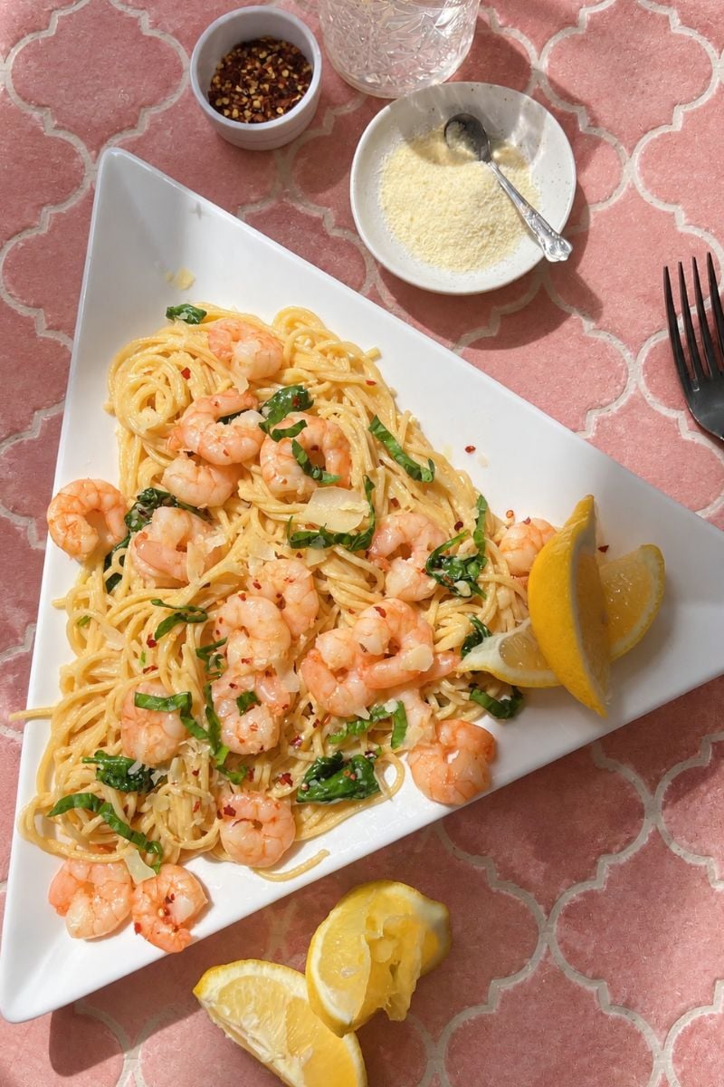 Creamy garlic butter shrimp pasta with spaghetti, baby spinach, Parmesan cheese, and red pepper flakes on a white plate.