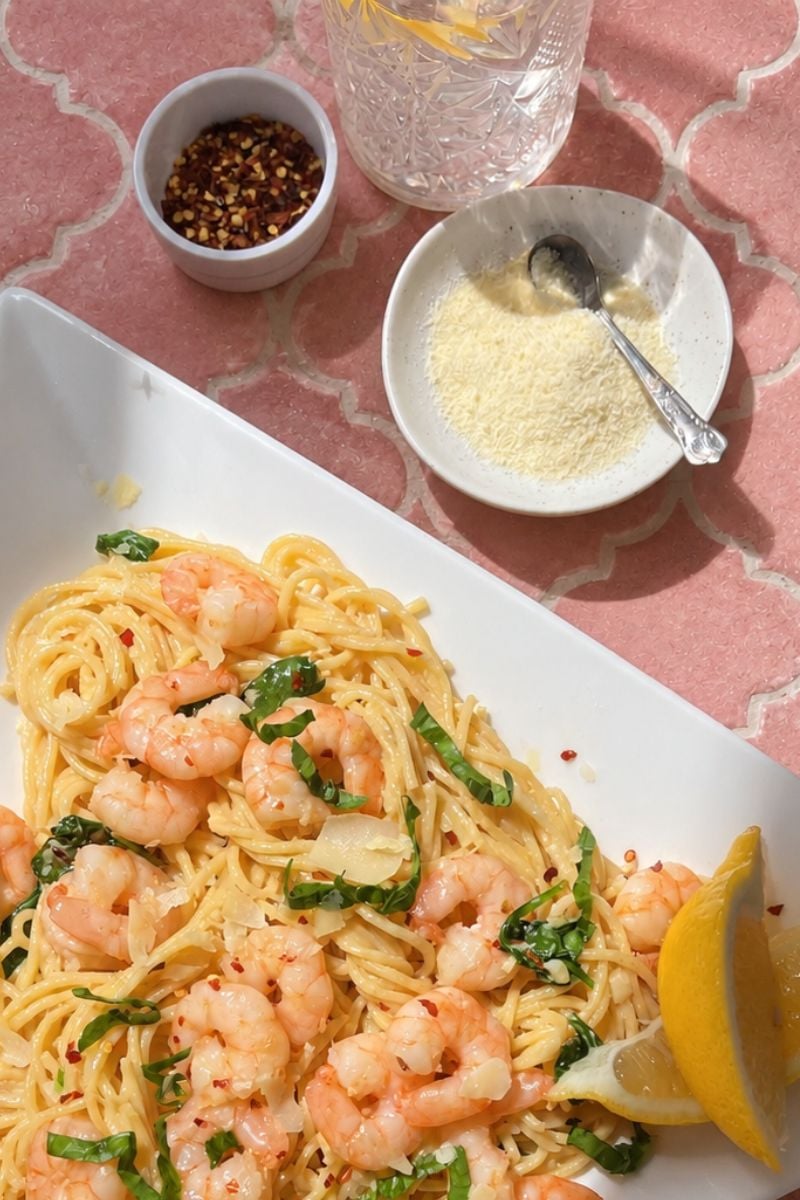 Creamy garlic butter noodles with shrimp, fresh baby spinach and Parmesan cheese on a white plate.
