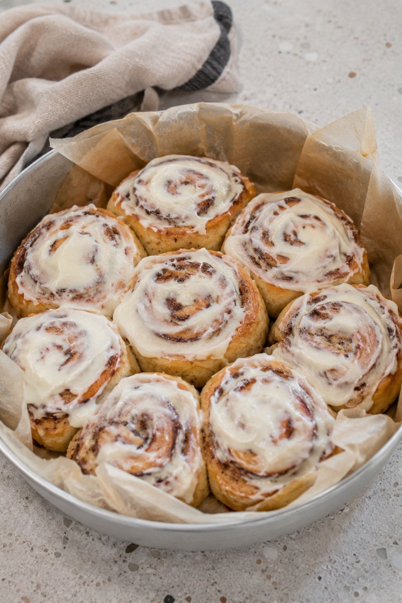 Easy no-rise cinnamon buns in a round container with cream cheese frosting.