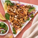 Crispy rice chicken salad with golden chicken, crunchy rice, fresh spinach, shredded carrots and red cabbage on a white serving plate.